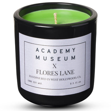 Green candle in a black container with a label on a white background FLORES LANE MOVIE GENRE CANDLES: SCI-FI MOVIE | ACADEMY MUSEUM